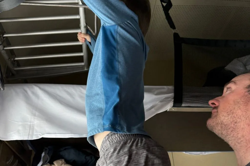 Child climbing the ladder to the top bunk of a sleeper train couchette with a parent spotting