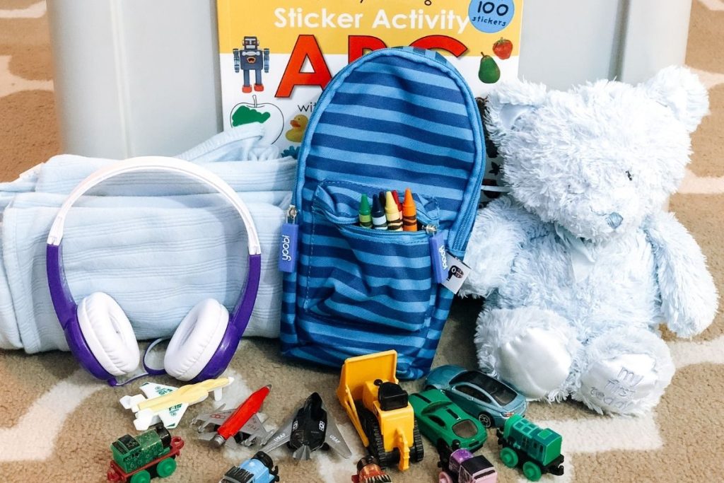 Child's carry-on backpack with headphones, sticker books, toy cars, stuffed animal, and change of clothes for airplane travel