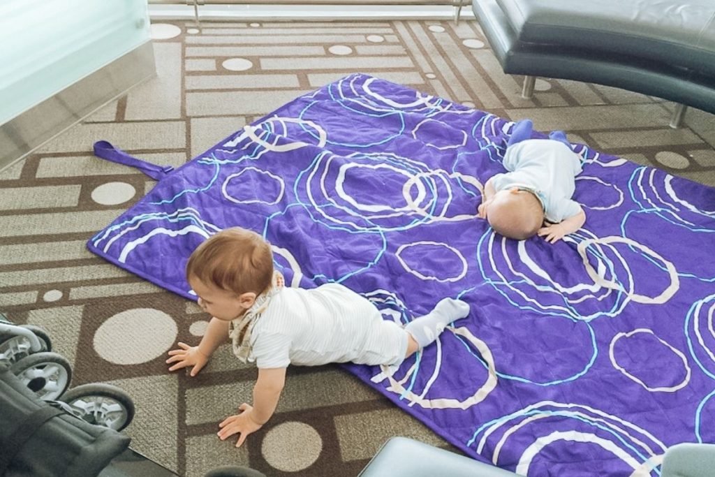 Twin babies sitting on picnic blanket on airport floor during layover