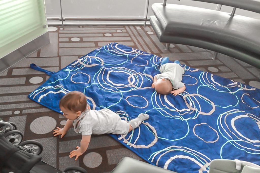 Twins having tummy time on picnic blanket at airport gate during layover